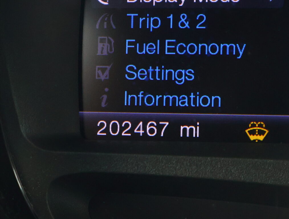 In-car display menu showing Trip 1&2, Fuel Economy, Settings; mileage 202,467 mi at bottom.