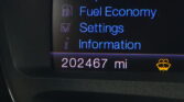 In-car display menu showing Trip 1&2, Fuel Economy, Settings; mileage 202,467 mi at bottom.