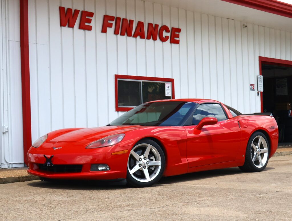Red sports car parked in front of a white building with red trim and a 'WE FINANCE' sign on the wall outside.