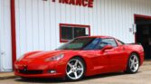 Red sports car parked in front of a white building with red trim and a 'WE FINANCE' sign on the wall outside.