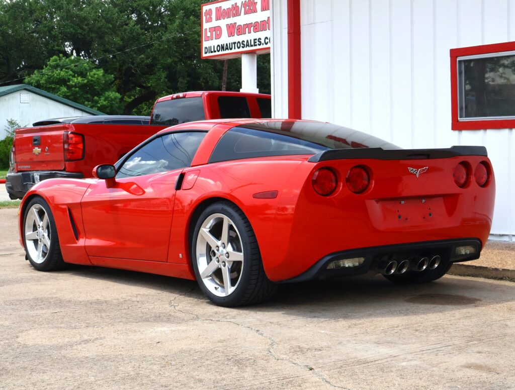 Red Chevrolet Corvette parked in front of a white building with red trim, showing its rear with quad exhausts.