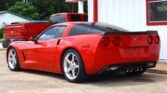 Red Chevrolet Corvette parked in front of a white building with red trim, showing its rear with quad exhausts.