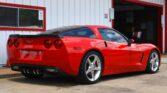 Red Chevrolet Corvette parked beside a white building with red window/door trim.