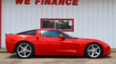 Bright red sports car parked in front of a white corrugated building with a large red 'WE FINANCE' sign above a window.