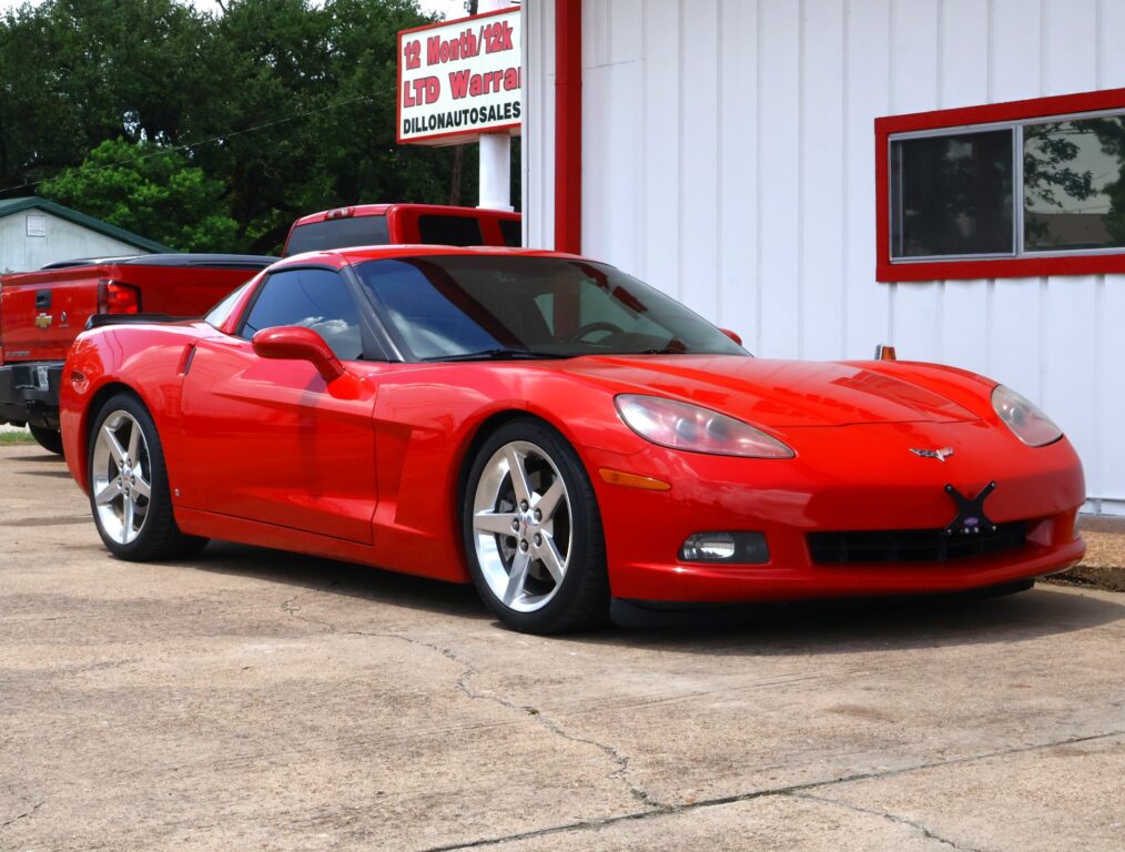 Red Chevrolet Corvette sports car parked in front of a white building with red trim and windows reflecting the surroundings.