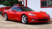 Red Chevrolet Corvette sports car parked in front of a white building with red trim and windows reflecting the surroundings.