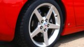 Close-up of a five-spoke silver alloy wheel on a red car, with a black tire and visible Corvette center emblem in the wheel.