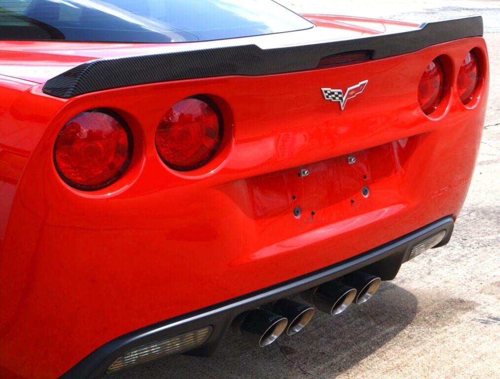 Rear view of a red Chevrolet Corvette with a carbon-fiber spoiler, quad exhausts, and round taillights.