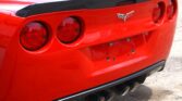 Rear view of a red Chevrolet Corvette with a carbon-fiber spoiler, quad exhausts, and round taillights.