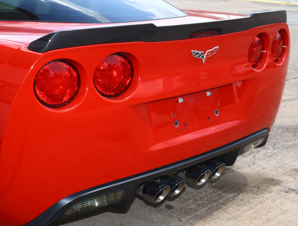 Rear view of a red Chevrolet Corvette with a carbon fiber spoiler, four round taillights, and quad exhausts.