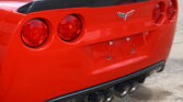 Rear view of a red Chevrolet Corvette with a carbon fiber spoiler, four round taillights, and quad exhausts.