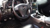 Close-up of a black leather car interior featuring a steering wheel with the Corvette emblem, dashboard gauges, and center console.