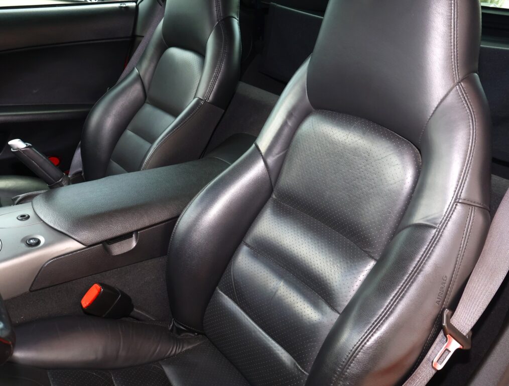 Black leather car seats in the front cabin with a center console and red seat belt buckles visible.