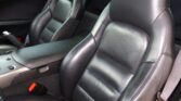 Black leather car seats in the front cabin with a center console and red seat belt buckles visible.