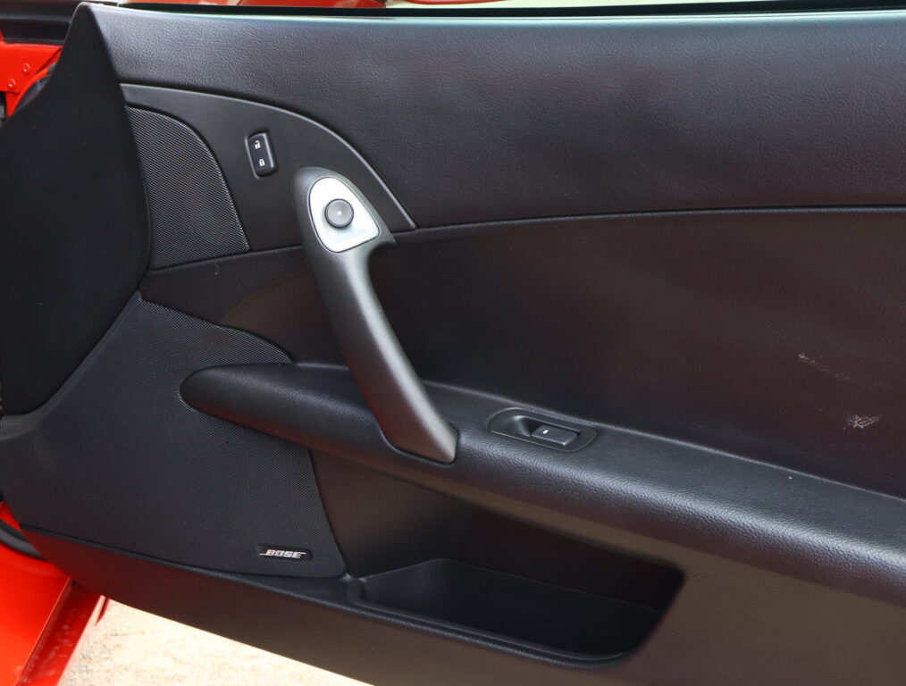 Interior of a car door: black panel with a visible Bose speaker badge, door handle, and window switch nearby.
