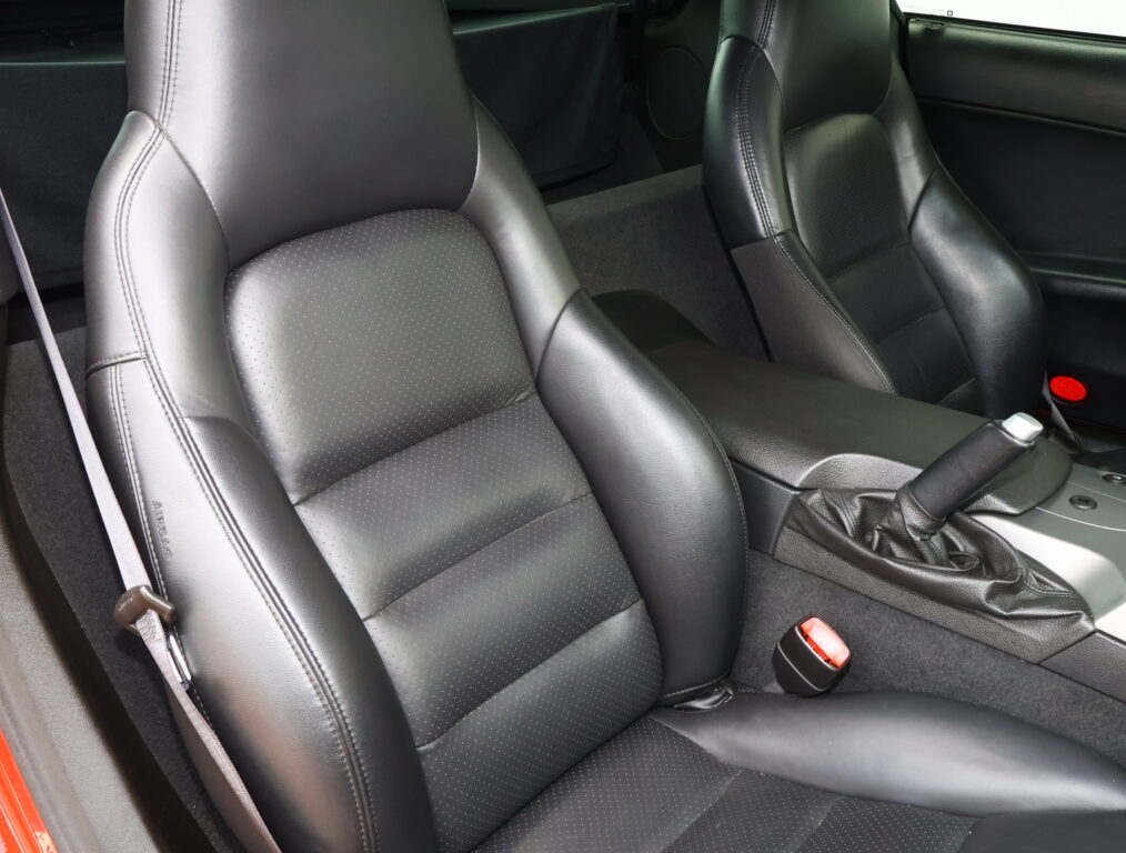 Close-up of black leather perforated front seats in a car interior with visible stitching and seat belt.