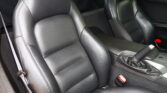 Close-up of black leather perforated front seats in a car interior with visible stitching and seat belt.