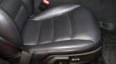 Close-up of a black leather car seat with a perforated pattern and a red seat belt buckle nearby.