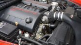 Close-up of a red Corvette engine bay, featuring the black engine covers with red 'CORVETTE' lettering and visible hoses.
