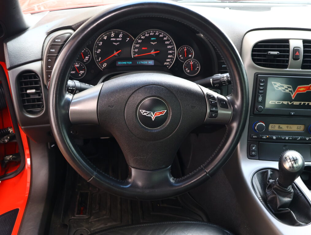 Close view of a car dashboard and steering wheel from the driver's seat, showing the speedometer, tachometer, and center console of a Corvette.