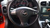 Close view of a car dashboard and steering wheel from the driver's seat, showing the speedometer, tachometer, and center console of a Corvette.