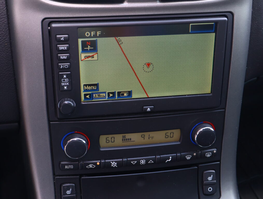 Car's navigation screen displaying a map with a red route line and a small compass overlay, surrounded by control buttons and climate dials on the dash.