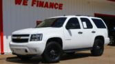 White Chevrolet Tahoe pickup/SUV parked in front of a white dealership building with a red WE FINANCE sign visible and a red trim edge.