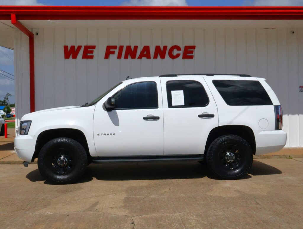 White Chevrolet Tahoe parked in front of a white storefront wall with a bold red WE FINANCE sign above.