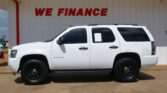 White Chevrolet Tahoe parked in front of a white storefront wall with a bold red WE FINANCE sign above.
