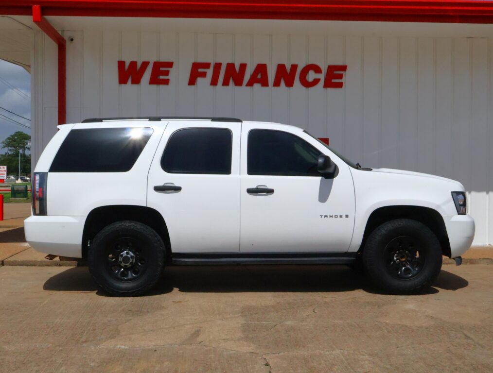 White Chevrolet Tahoe parked in front of a building with a red 'WE FINANCE' sign on the wall behind it