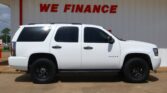 White Chevrolet Tahoe parked in front of a building with a red 'WE FINANCE' sign on the wall behind it