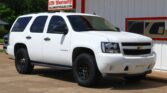 White Chevrolet Tahoe parked in front of a building with bold red 'WE FINANCE' lettering and dealership signs in the background.