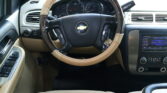 Beige-car interior with a wood-trim steering wheel and gauges behind it, including the speedometer and tachometer, in view of the dashboard center console.