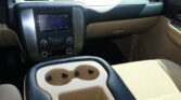 Interior of a car showing the center console with two beige cup holders and a touchscreen infotainment panel nearby (driver's side).