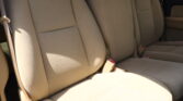 Beige car back seat with three seating areas and visible seat belts, interior upholstery in sunlight.