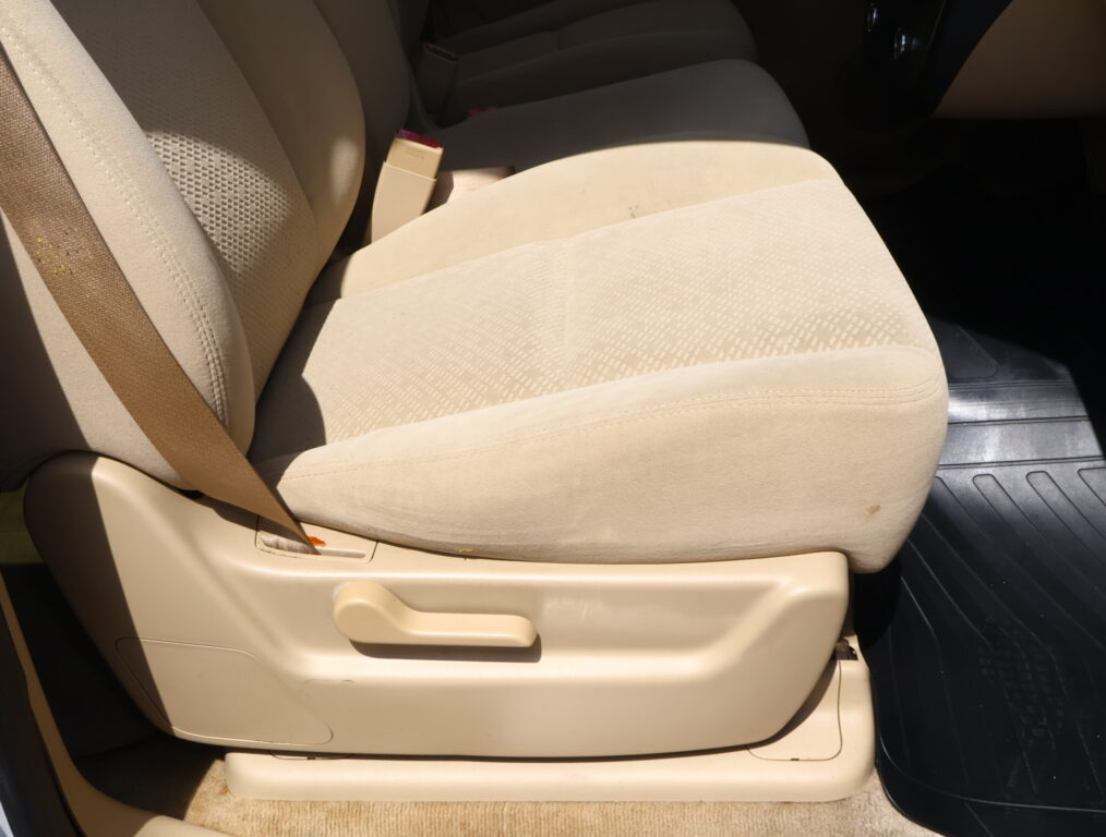 Beige car seat with integrated seatbelt buckle and floor mat visible in the passenger area of a vehicle.