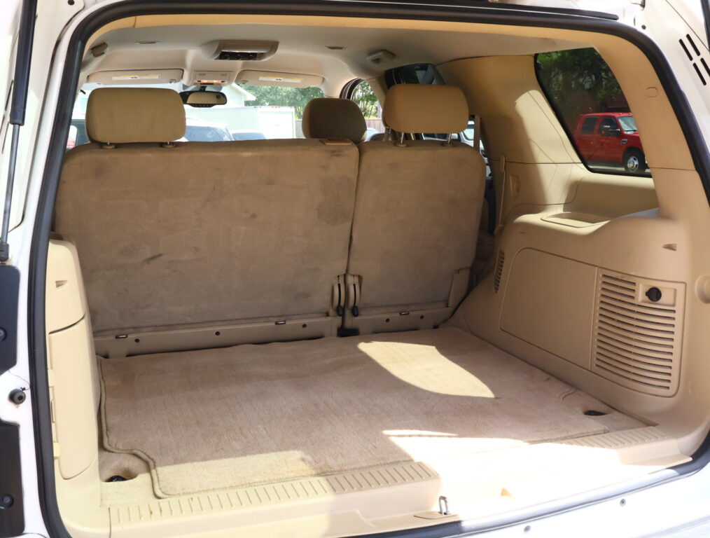 Open rear hatch view of a beige SUV interior with the third-row seats upright and folded cargo area behind them.