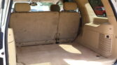 Open rear hatch view of a beige SUV interior with the third-row seats upright and folded cargo area behind them.