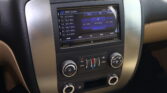 In-car touchscreen displaying FM radio interface with presets, frequencies, and blue control panels, surrounded by silver dashboard trim.